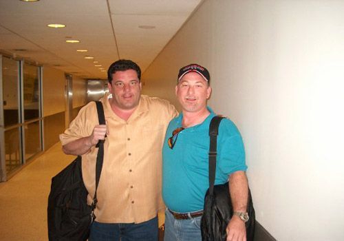 Two men are posing for a picture in a hallway.