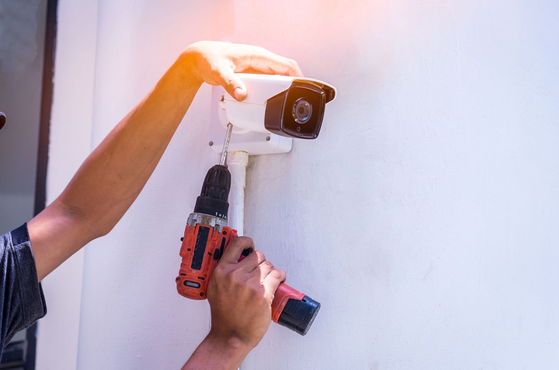 A man is installing a security camera on a wall with a drill.